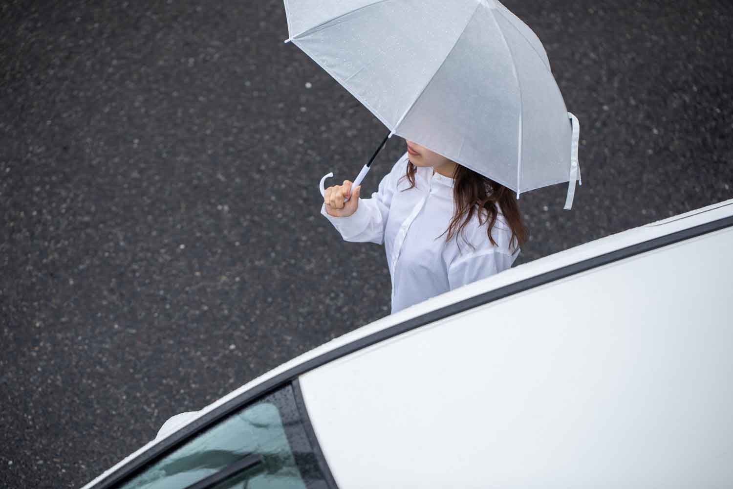 傘を持った女性がクルマ沿いに歩行している様子
